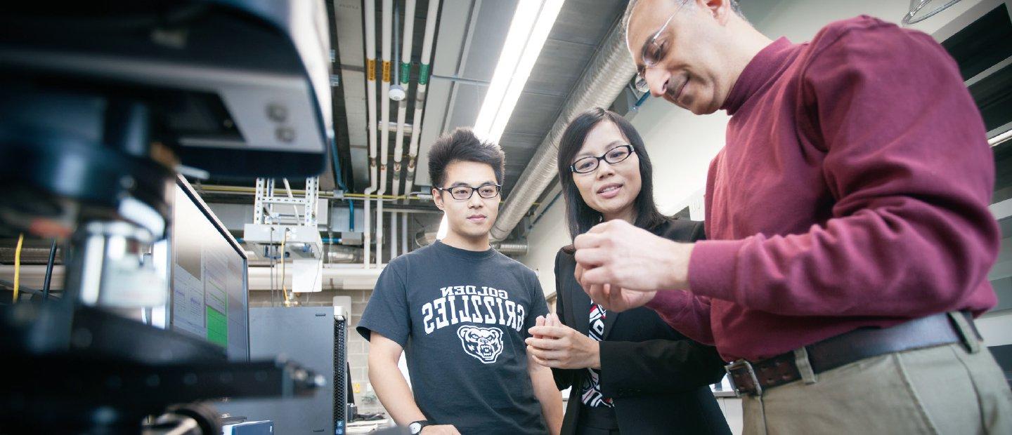 一名男子在实验室向两名学生展示一个小型机械装置